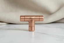 Load image into Gallery viewer, Copper T-shaped handle on a white surface with a beige fabric background