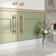 Load image into Gallery viewer, Kitchen with green cabinets, copper handles, and a vase of flowers on the counter.
