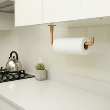 Load image into Gallery viewer, Copper pipe paper towel holder on a kitchen wall with a stove and plant in the background.