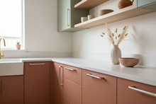 Load image into Gallery viewer, Modern kitchen with brown cabinets, white countertops, and decorative elements.