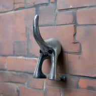 A solid cast iron coat hook with a dog tail design, mounted on a brick wall.