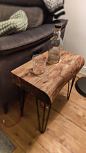 Load image into Gallery viewer, Acacia wood Table top with a live edge and black hairpin legs, next to a grey sofa. A bottle of whiskey and glass on the table top in a dimly lit room