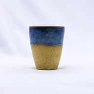 Ceramic cup with blue top and beige bottom on a white background