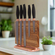 A stylish wooden knife block holds five sleek knives with black handles and copper accents, set on a kitchen countertop with greenery.