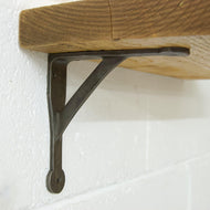 Close-up of a sturdy metal shelf bracket supporting a wooden shelf against a textured white wall.