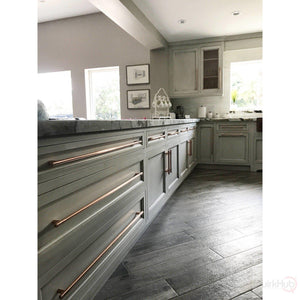 Handmade copper T Bar handles on large grey kitchen drawers and doors in a well lit kitchen 